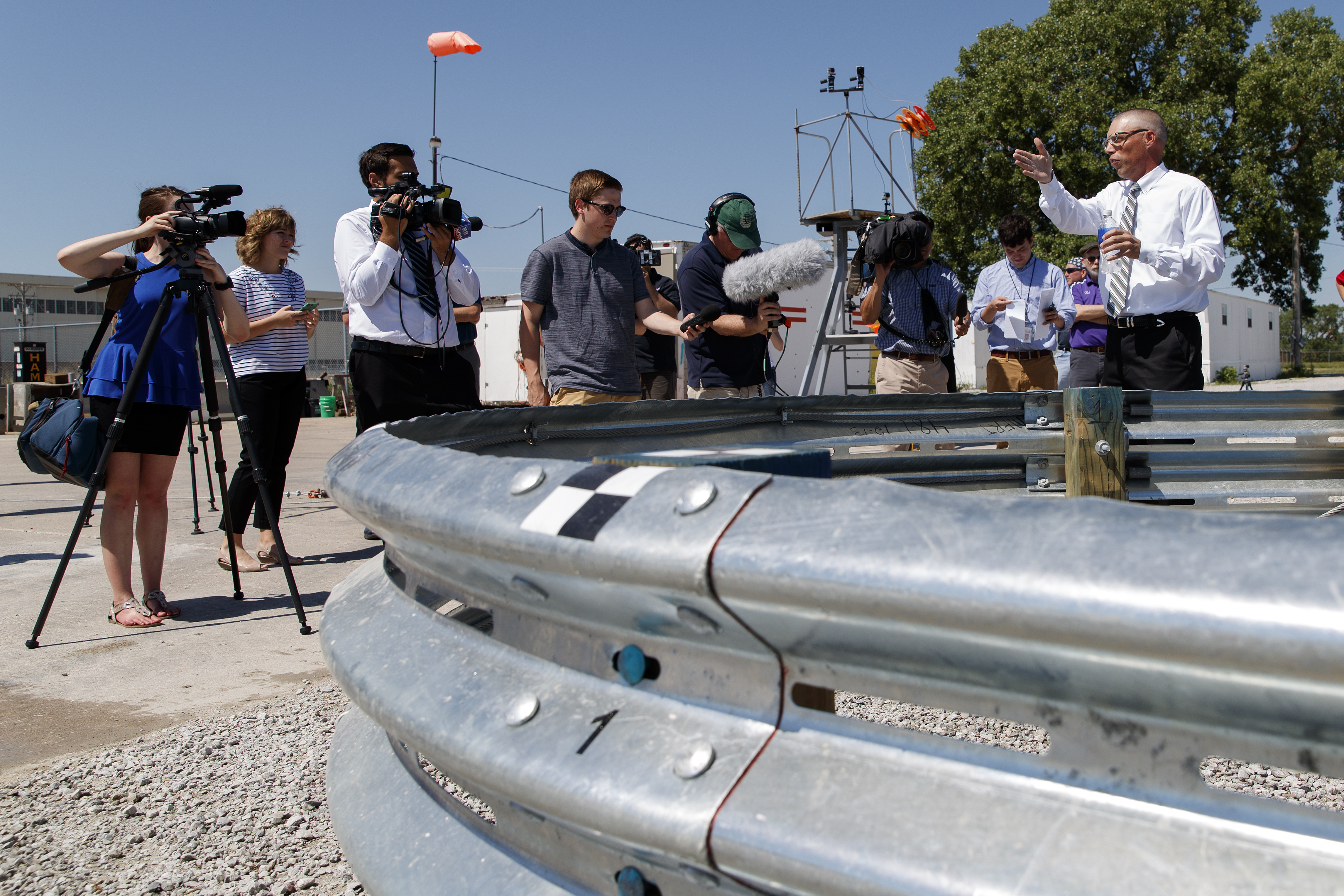 Bob Bielenberg (right) explains the new highway barrier being tested to the media and the NASCAR tour group.