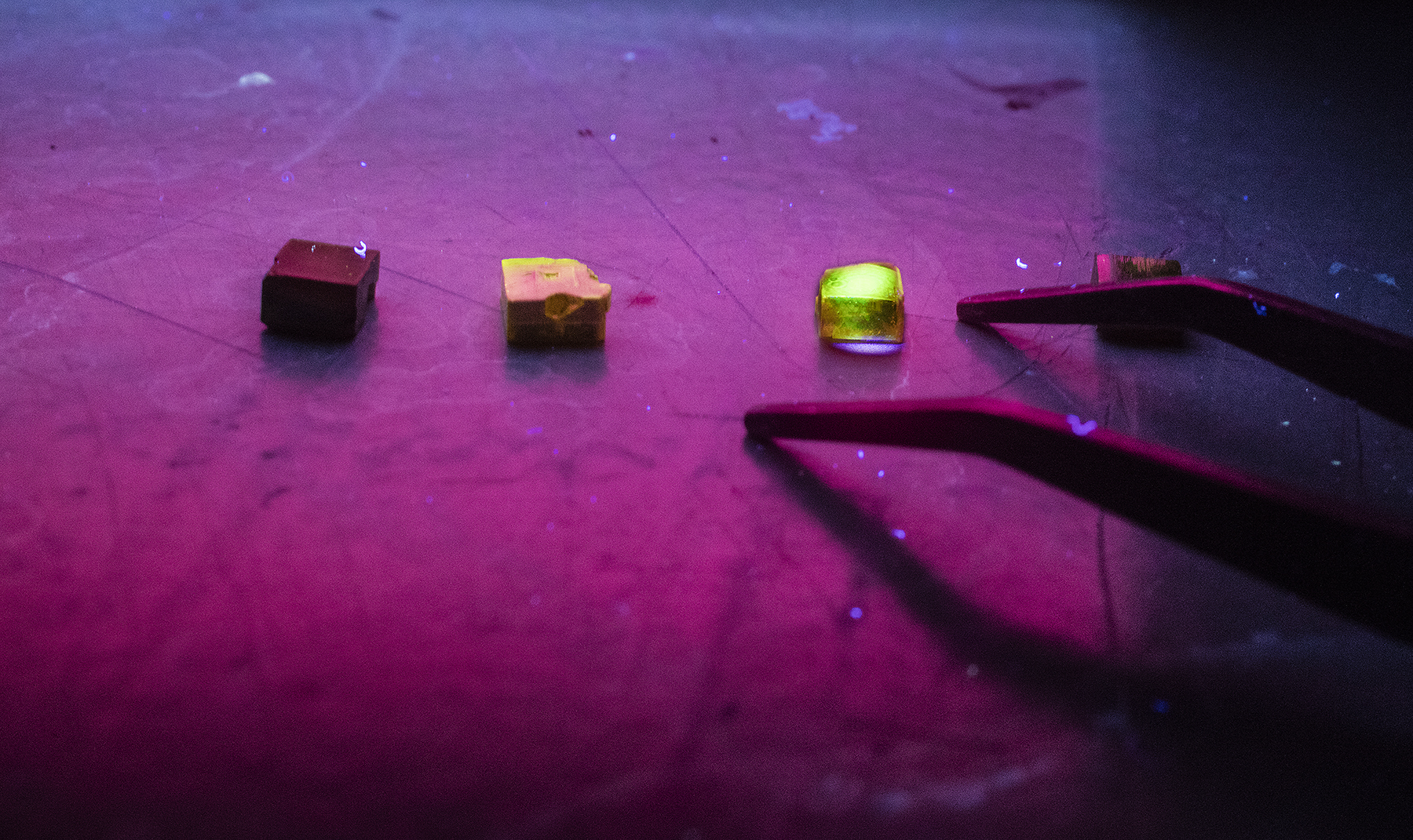 Three crystals of methylammonium lead tribromide are illuminated by ultraviolet light. High-quality crystals suitable for X-ray detection glow green when struck by an ultraviolet laser, as illustrated by the crystal at far right.