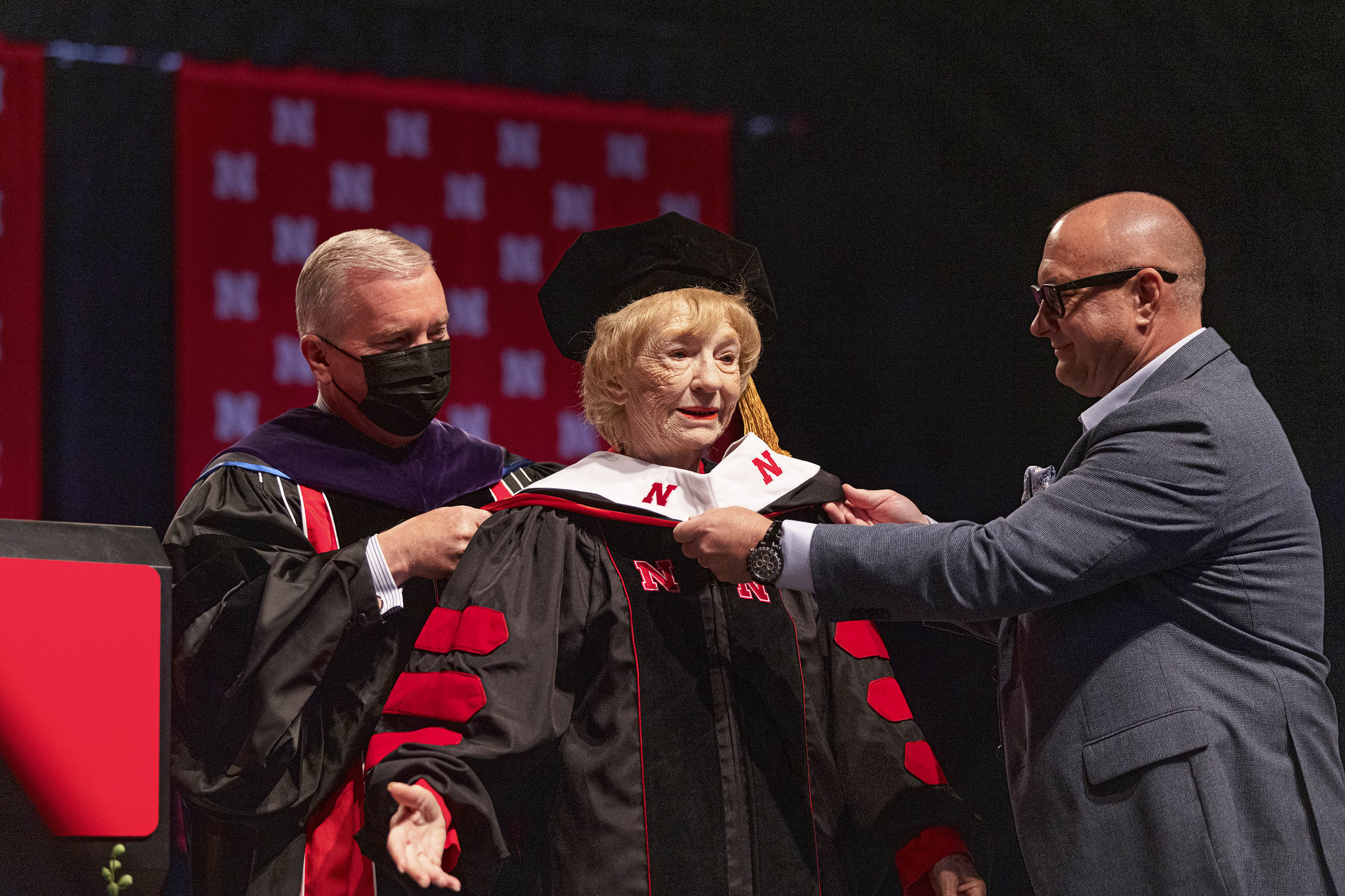 Leta Powell Drake, local television pioneer and Husker alumna, is hooded by University of Nebraska Regent Tim Clare (left) and her son, Aaron (right), during the University of Nebraska–Lincoln’s undergraduate commencement ceremony Aug. 14 at Pinnacle Bank Arena. The university presented Drake with an honorary Doctor of Humane Letters during the ceremony.