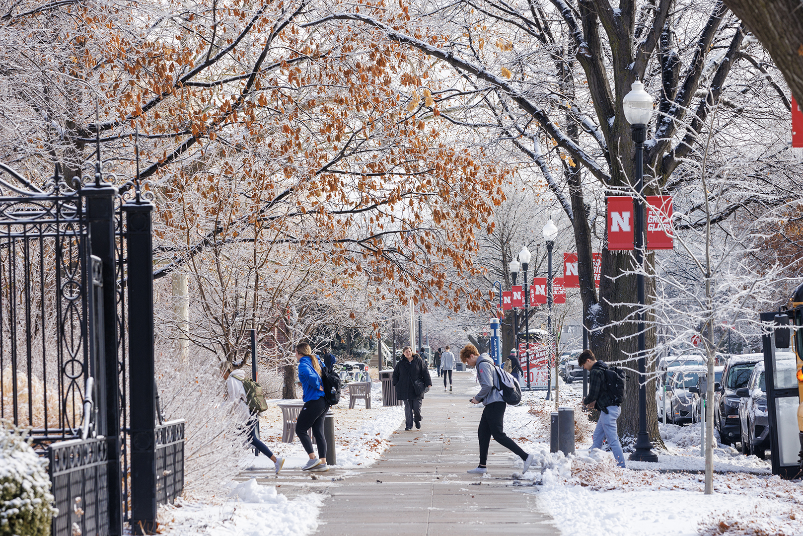 University of Nebraska–Lincoln students walk on a sidewalk near Louise Pound Hall, with snow covering the ground and tree branches.