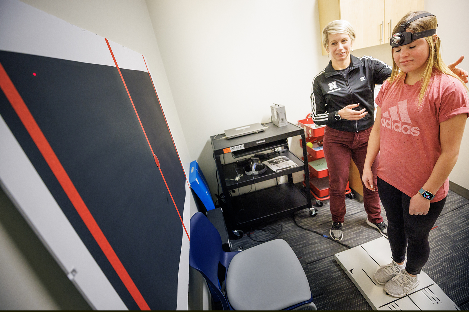 Dr. Kate Higgins, an athletic neuropsychologist with Husker Athletics, performs a concussion balance test on mock patient Makayla Burchett, a freshman from Harlan, Iowa. Burchett wears a laser pointer as she moves her head around a target on the wall while balanced on a force plate. Nebraska Medicine recently moved its concussion clinic to the Nebraska Athletic Performance Lab in Memorial Stadium.