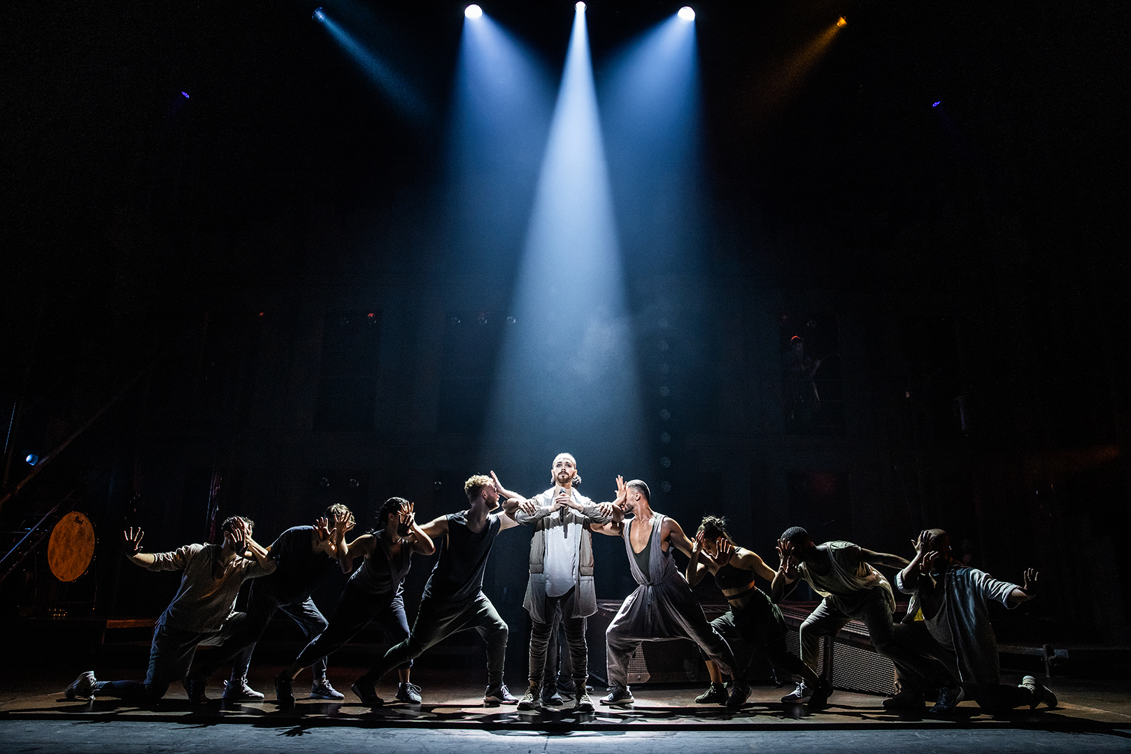 A "Jesus Christ Superstar" cast member stands in a spotlight, with four people striking poses on each side.