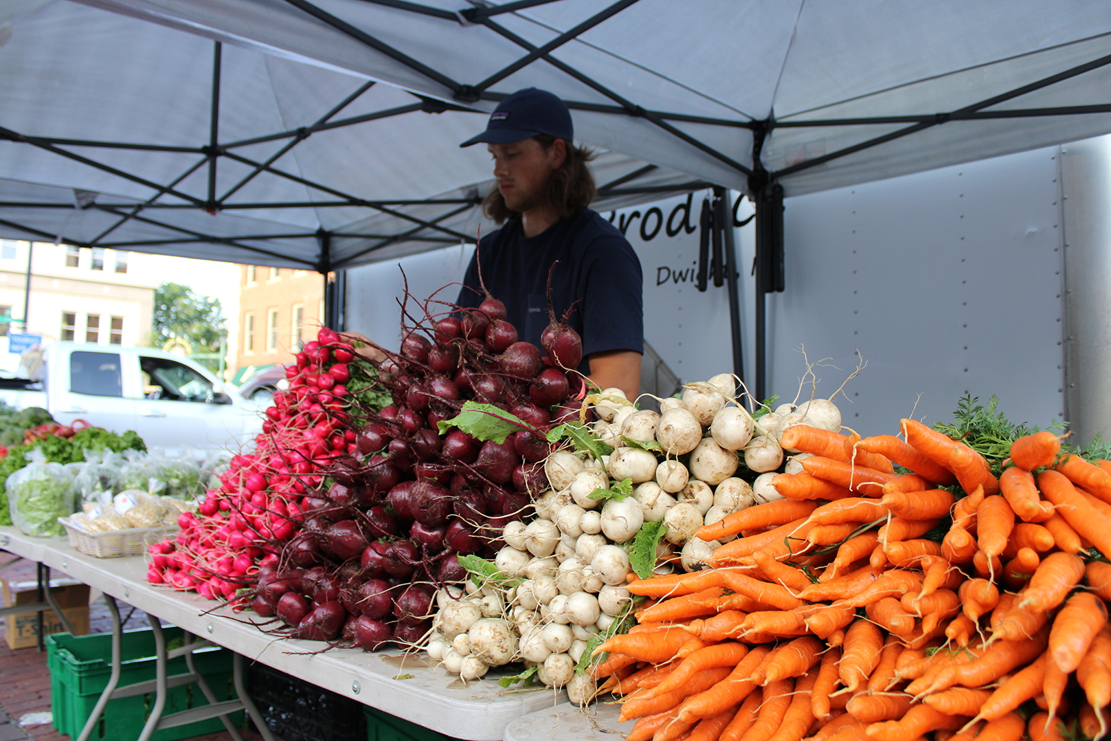 A young man stands behind a table stacked with vegetables.