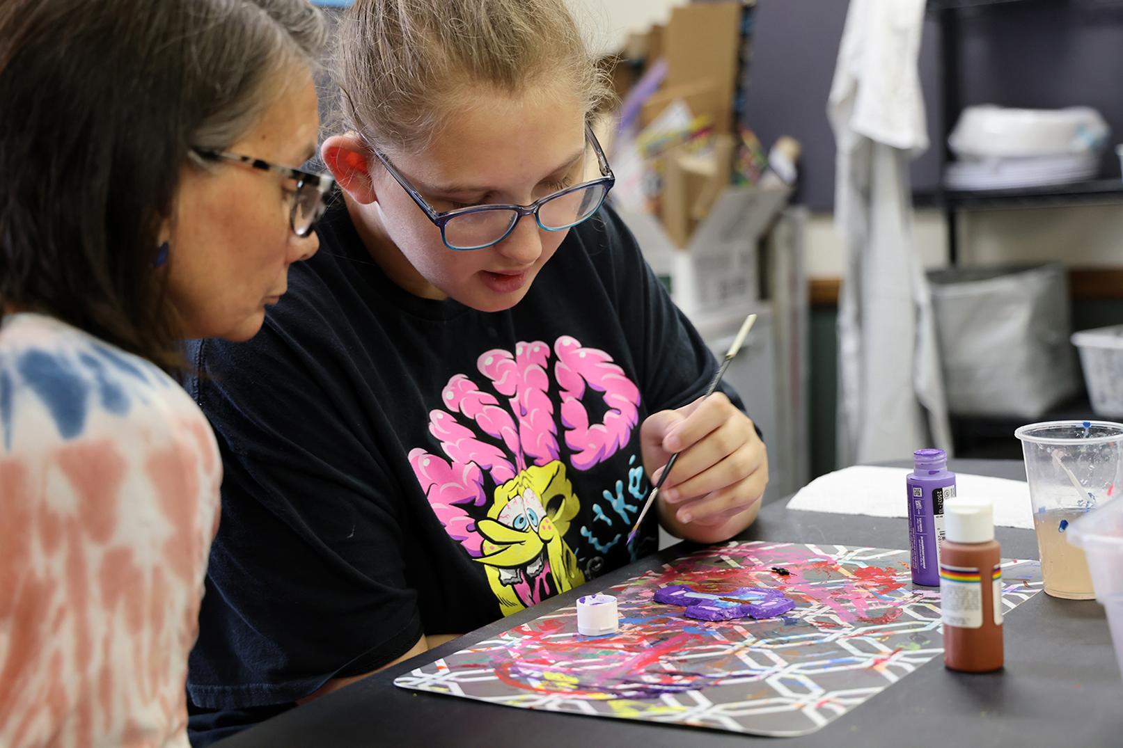 Zoe Johnson paints a wooden cross with the help of an Our Place teacher.