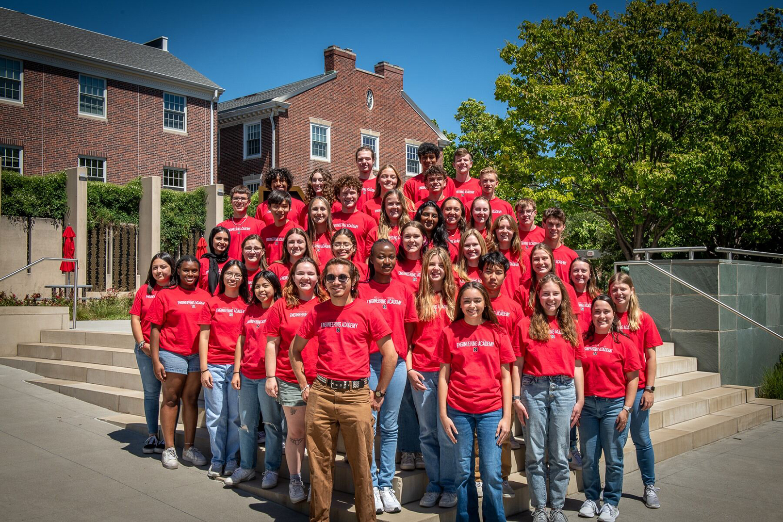 A large group of Nebraska Engineering students, wearing red T-shirts, stands outside of the Wick Alumni Center.