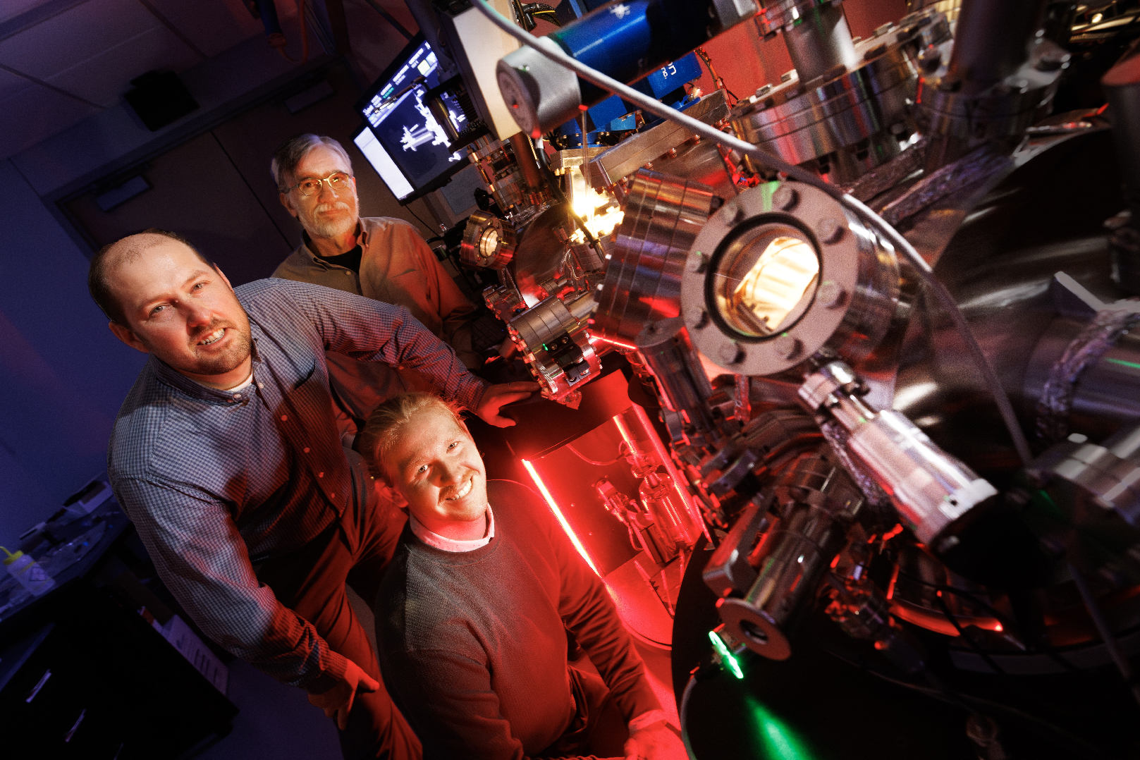 Craig Zuhlke, George Gogos and Graham Kaufman pose with the Leybold ultra-high vacuum laser surface processing and materials analysis system in the Engineering Research Center.