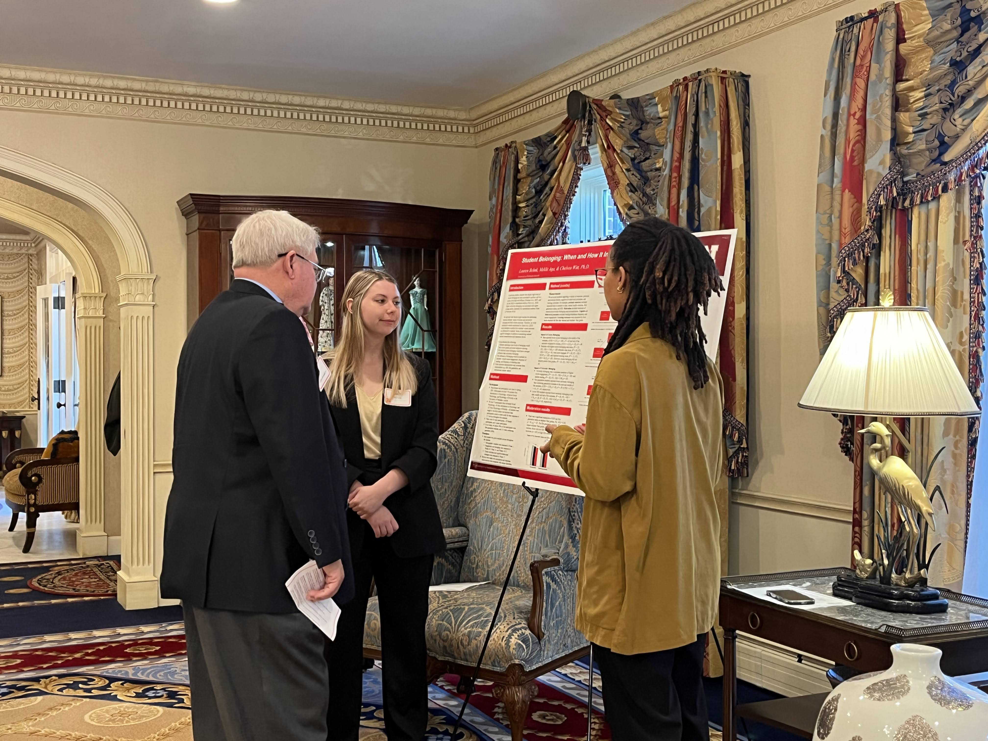 Seniors Lauren Behnk (center) and Meklit Aga (right) present their research poster to State Sen. Rick Holdcroft (left).