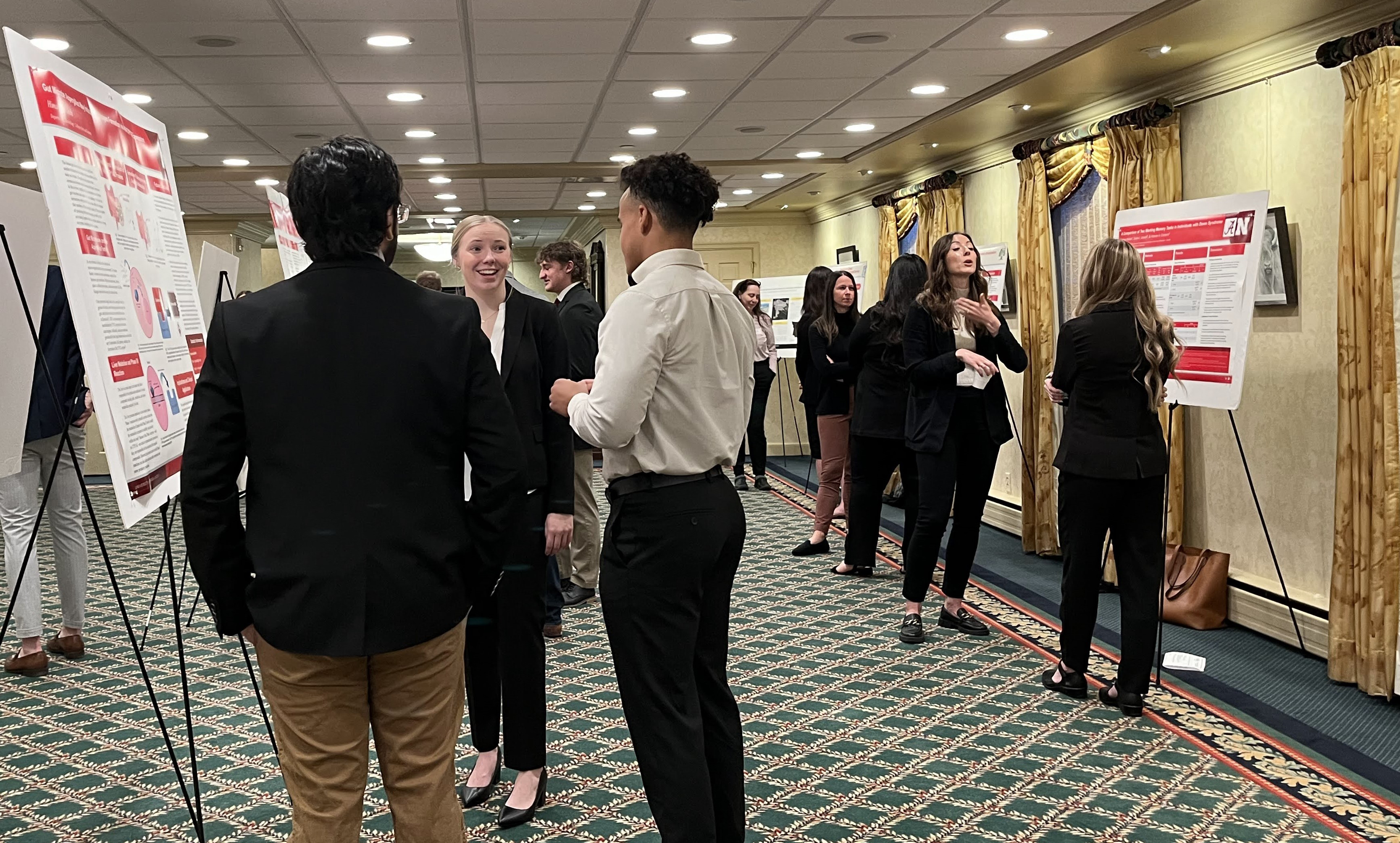 About a dozen college students stand next to their research posters in the Nebraska Governor's Mansion.