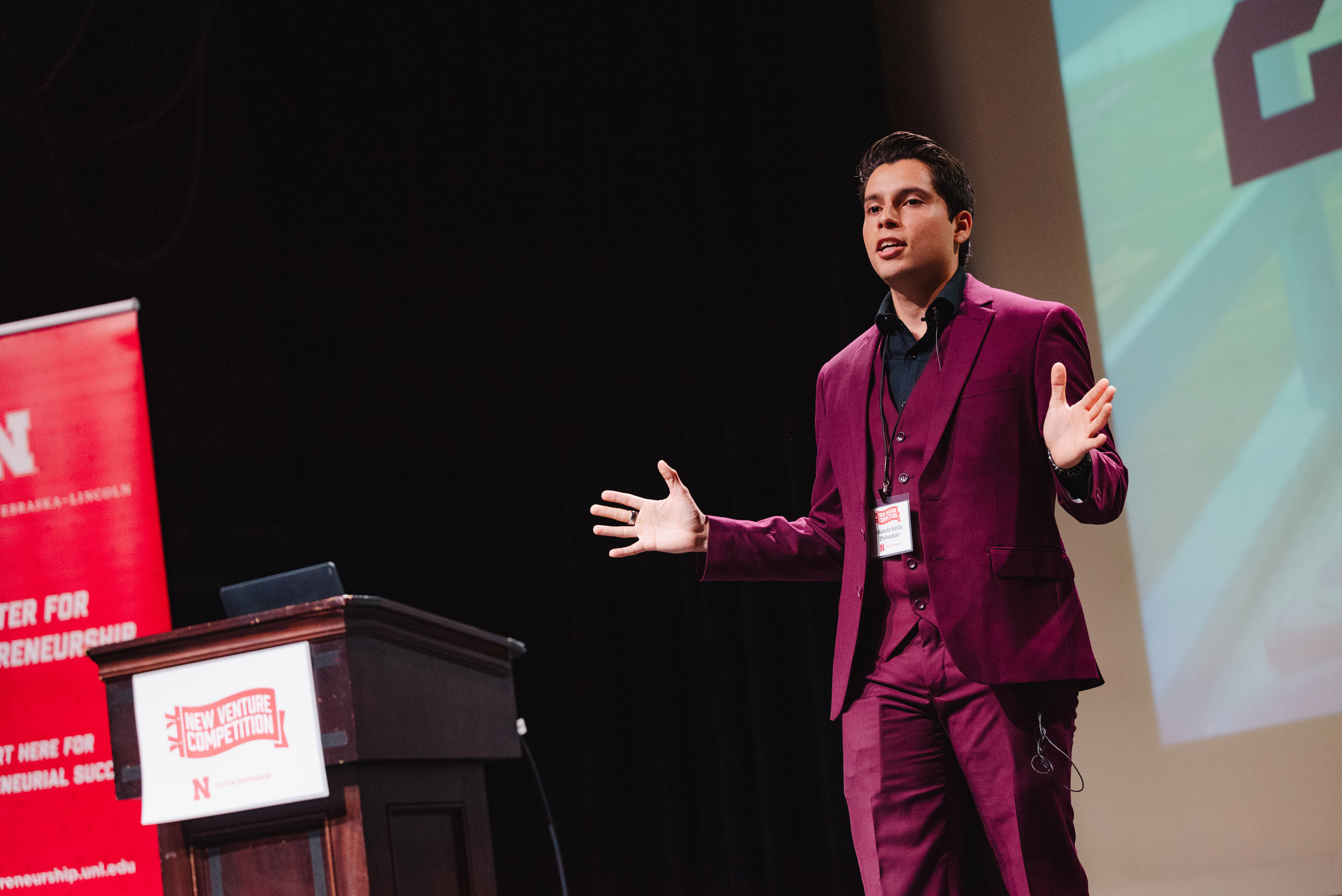 A young man in a maroon suit speaks on stage.