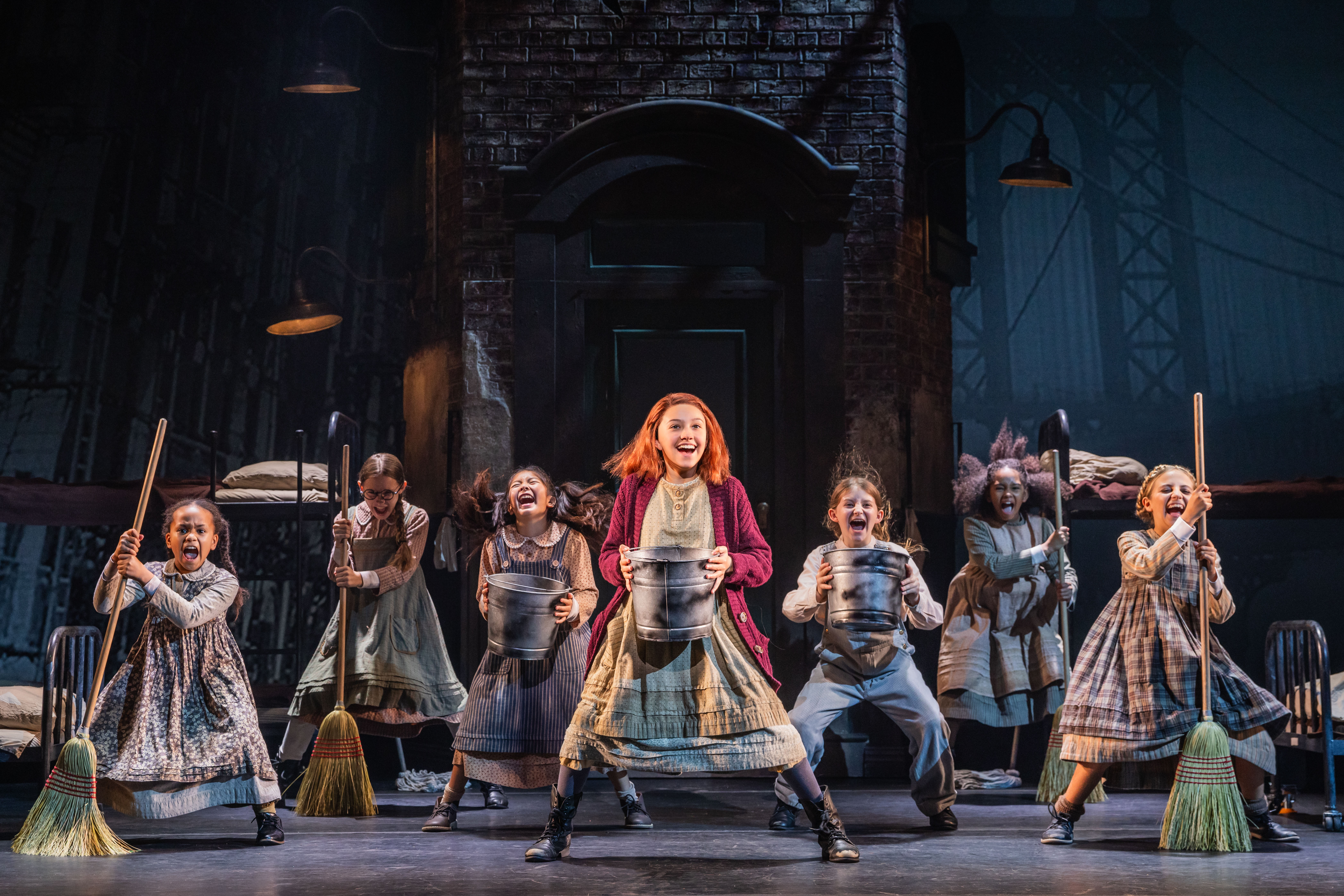 Seven young girls, dressed as orphans, dance with buckets and brooms onstage.