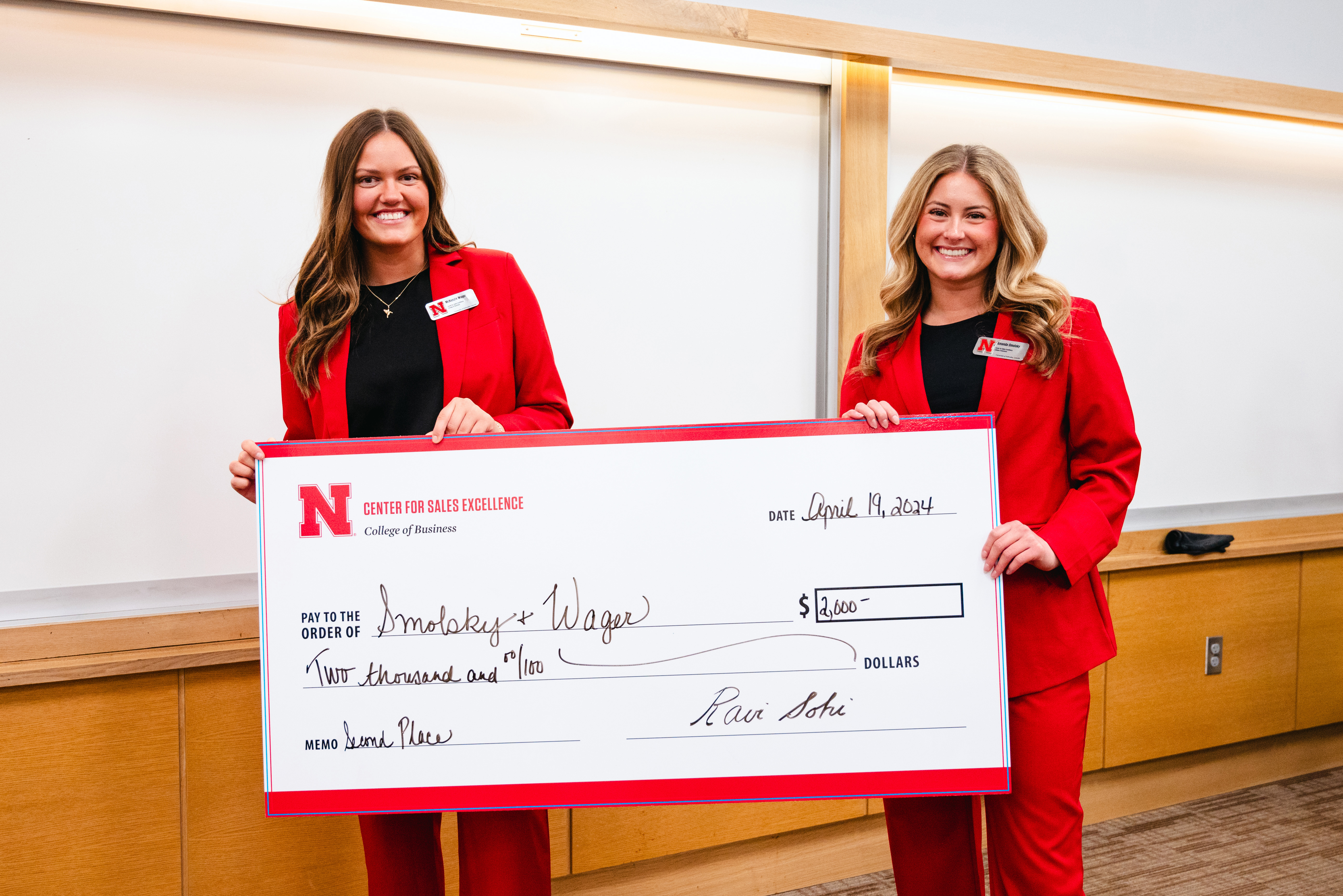 Two young women hold an oversized check for $2,000.