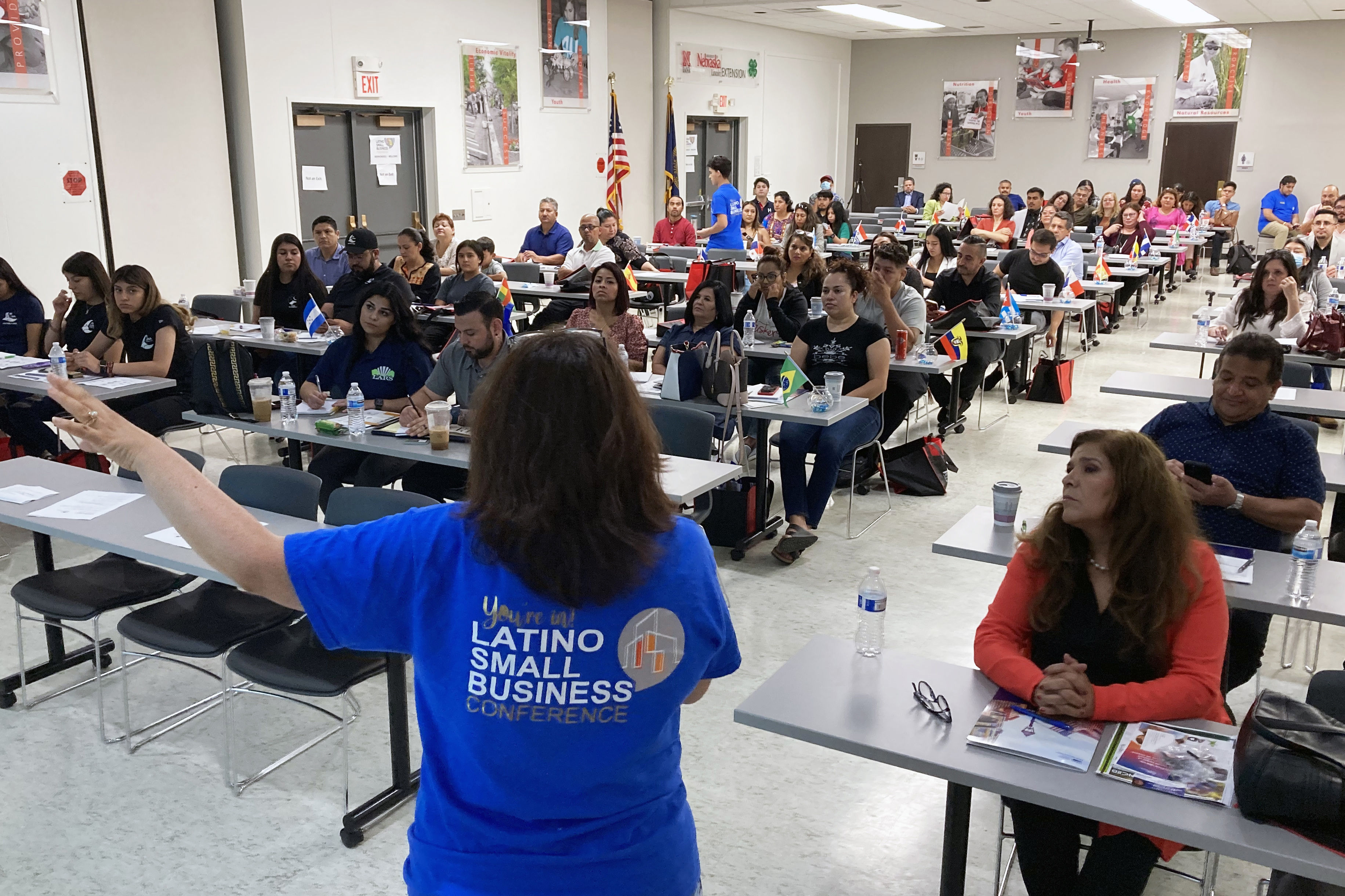 Sandra Barrera speaks in front of a crowd of a few dozen Latinx entrepreneurs, seated at tables.