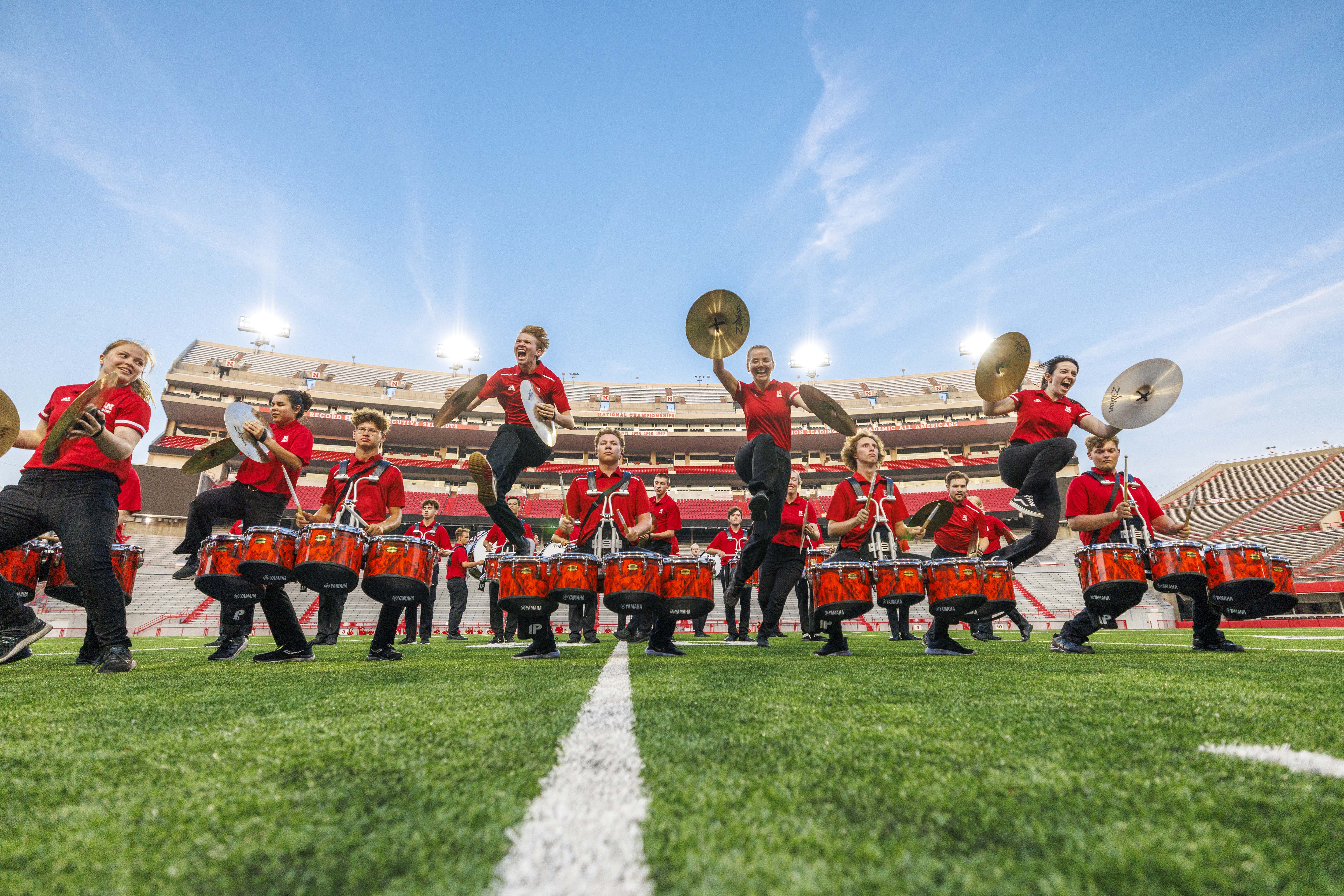 The Cornhusker Marching Band cymbal line jumps over the quad line during the battery’s individual performance during the Cornhusker Marching Band's annual exhibition concert Aug. 23 at Memorial Stadium.