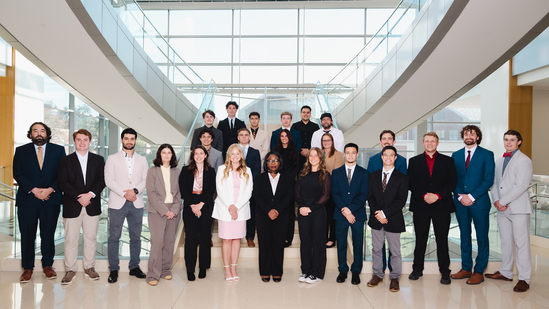 Twenty-four people in formal wear pose for a photo on a staircase in Howard L. Hawks Hall.