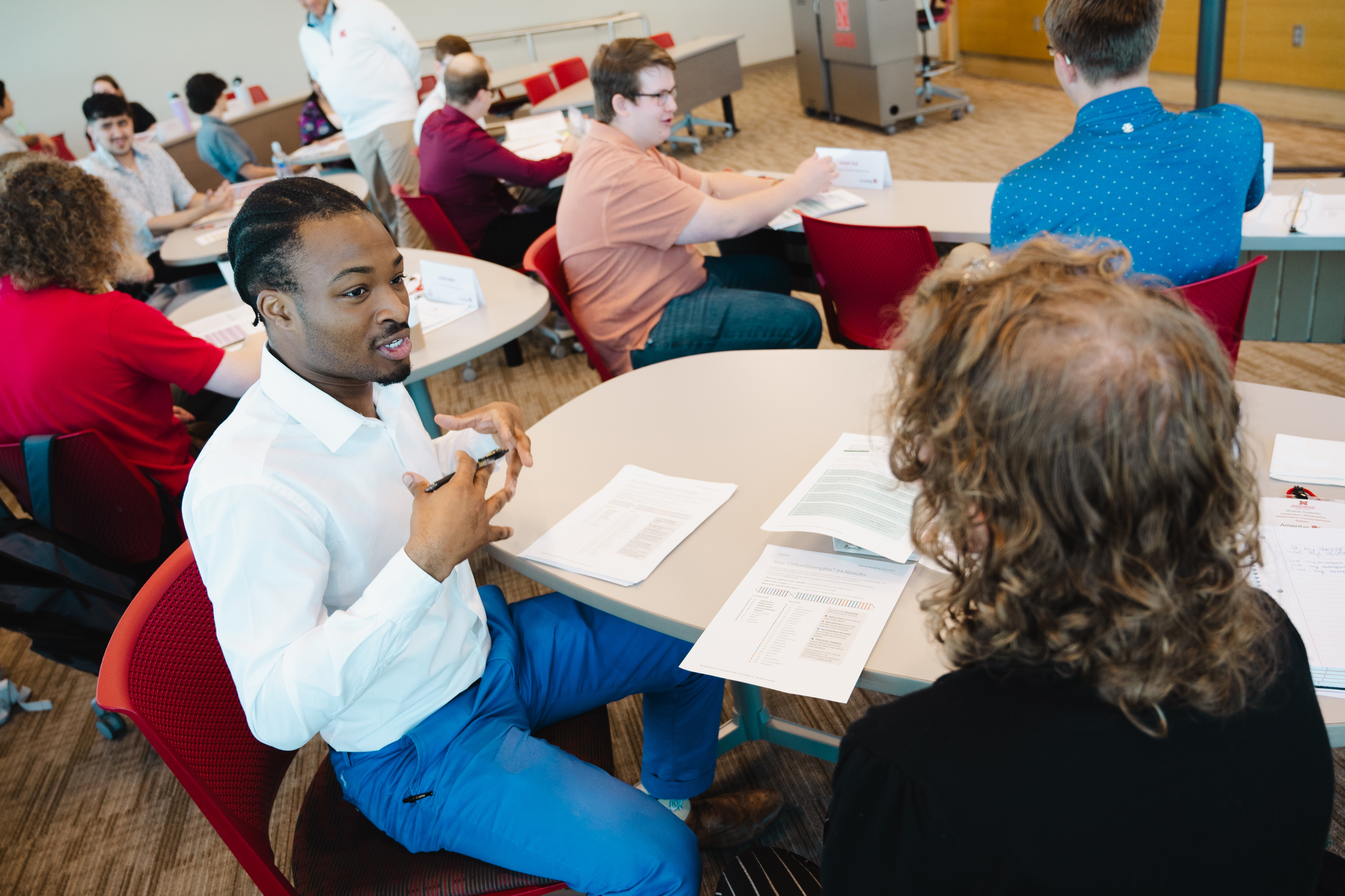 A dozen or so people converse at small tables in a classroom.