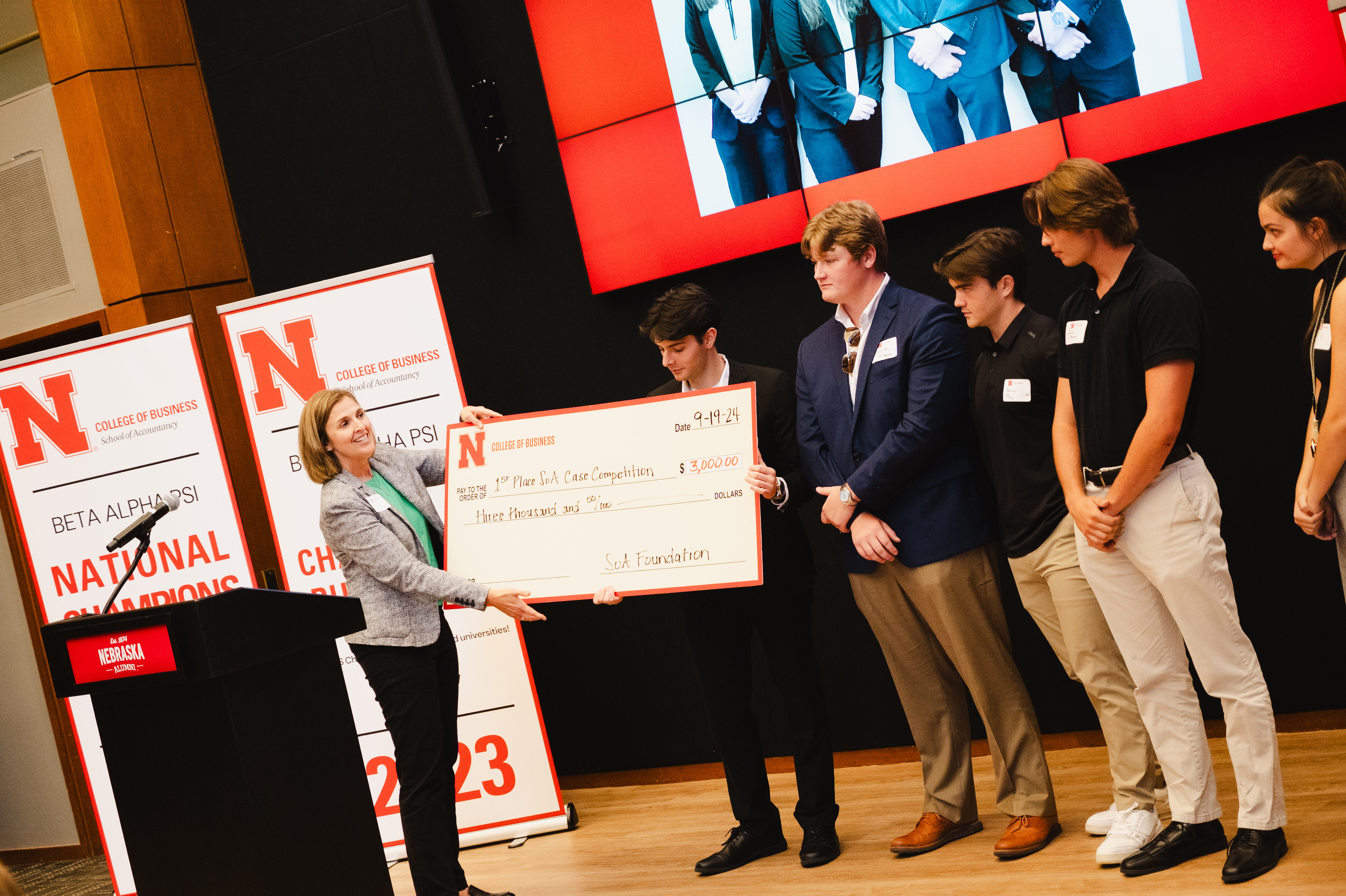 Jill Trucke, associate professor of practice in accountancy, awards a large $3,000 check to a Husker student, while four other students stand on stage.