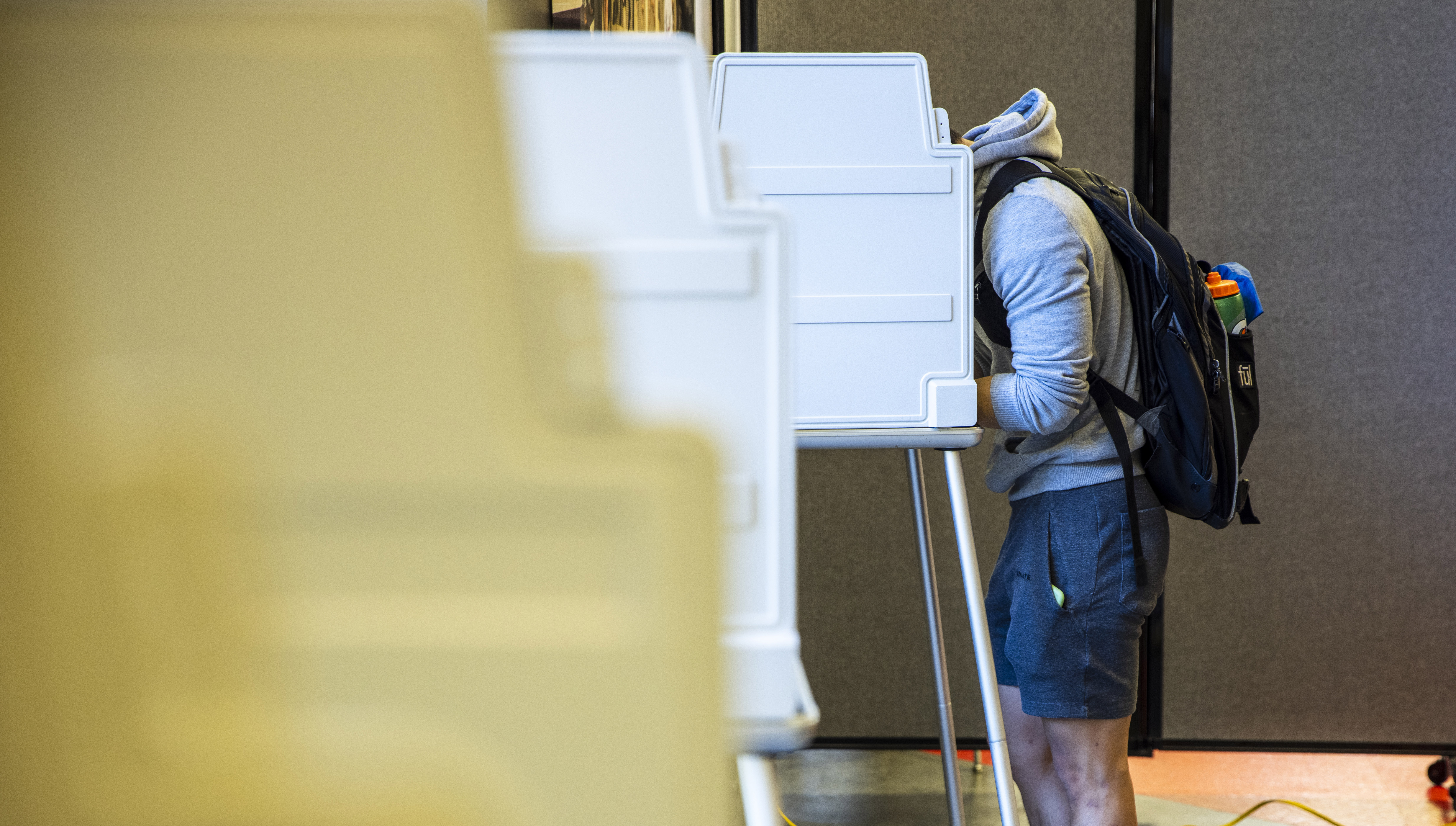 A male student with a backpack votes in a booth.