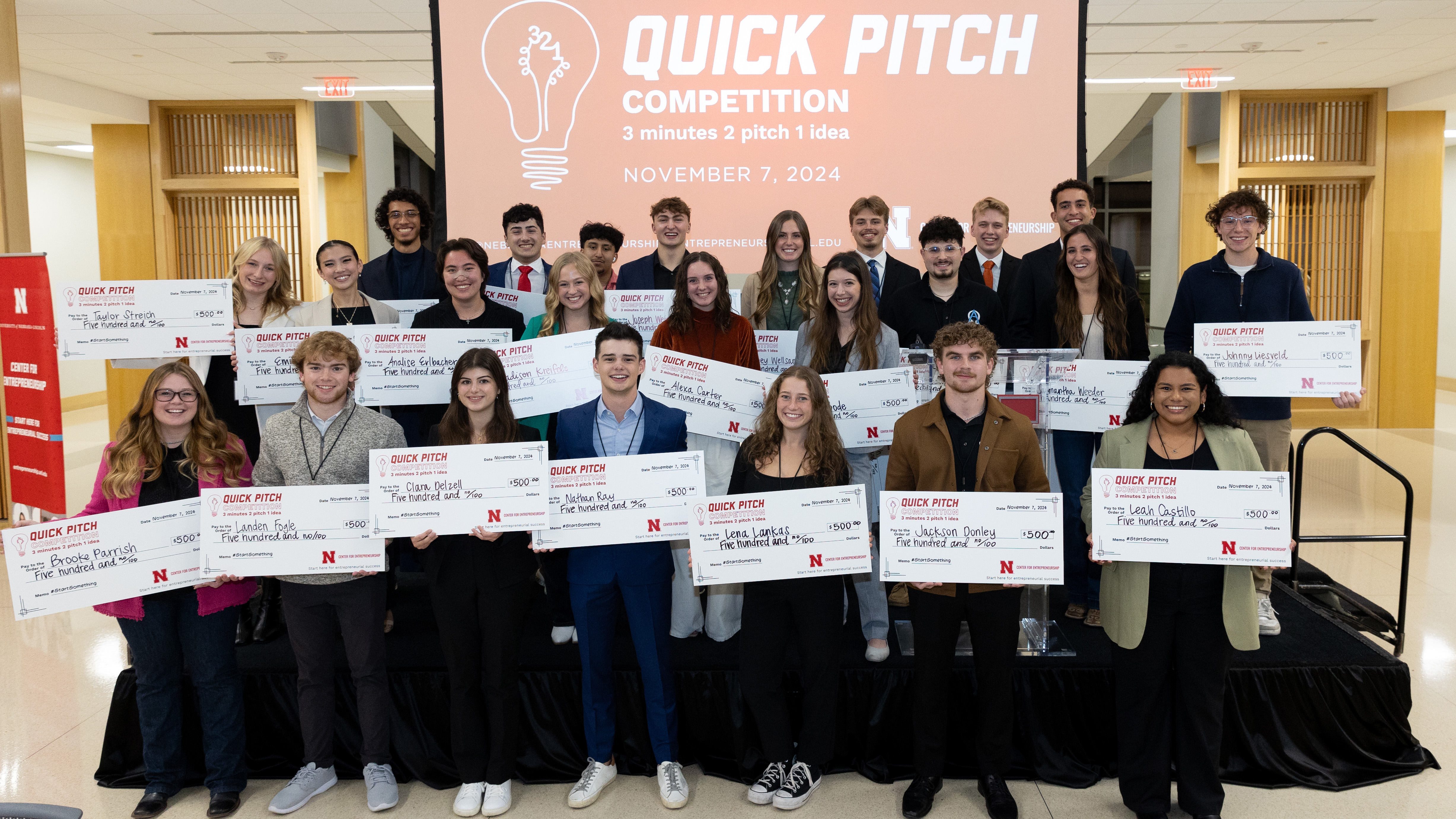 The 24 winners of the 3-2-1 Quick Pitch competition pose with giant checks of $500 each.