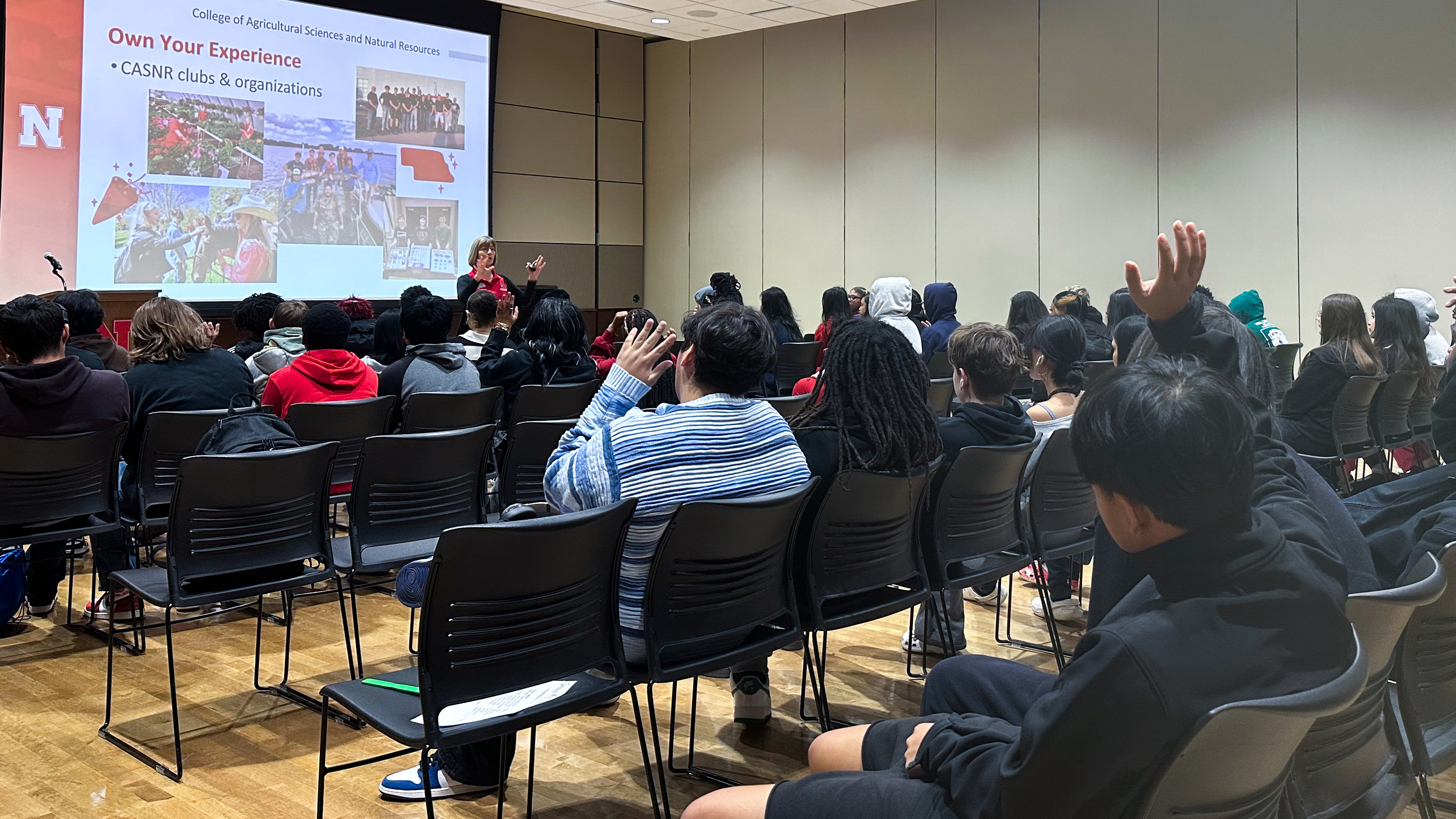 Sue Ellen Pegg, recruitment coordinator with the College of Agricultural Sciences and Natural Resources, speaks in front of at least three dozen high school students, seated in chairs. Two students have their hands raised.