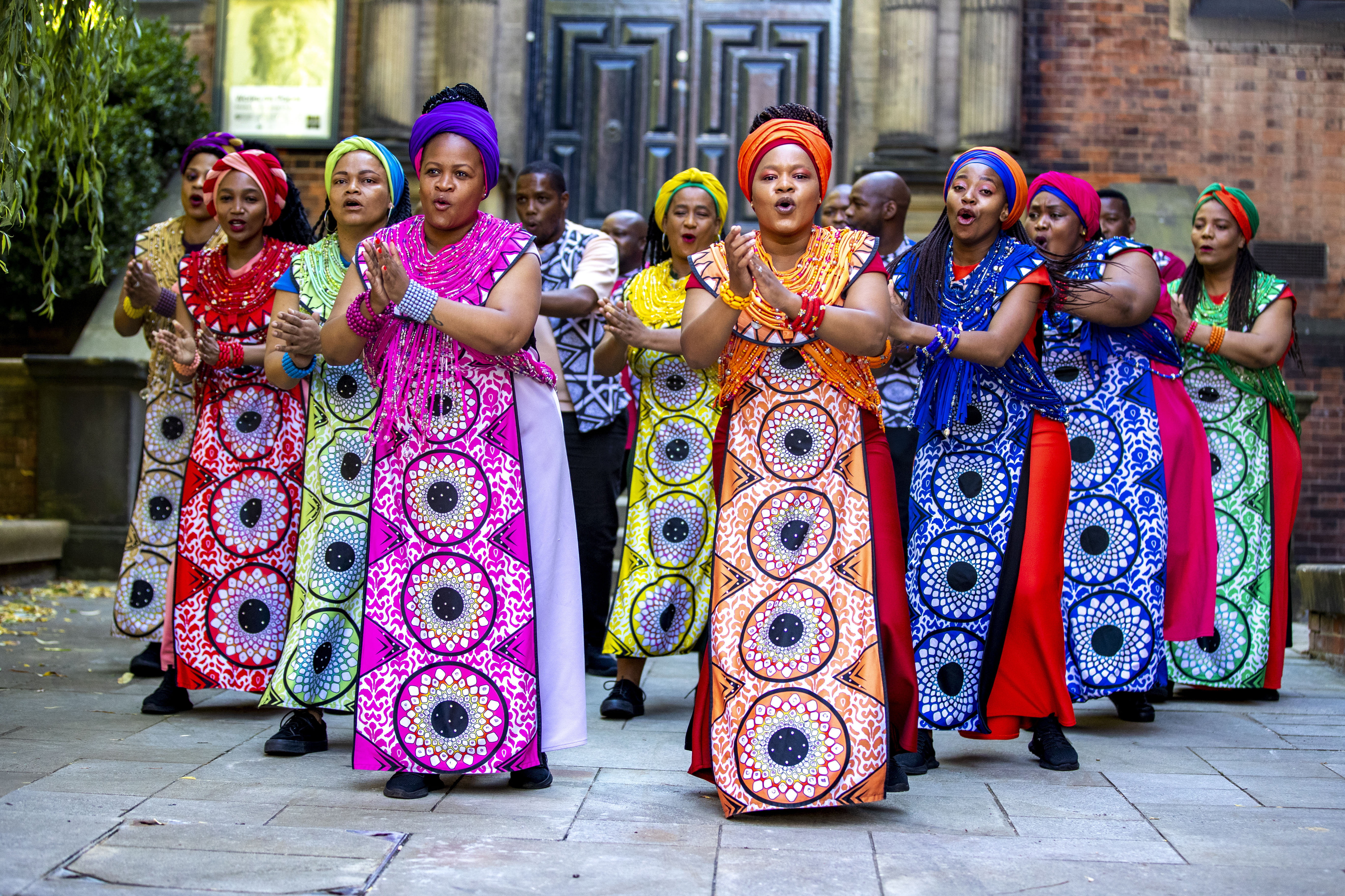 African-American women sing while wearing colorful dresses.