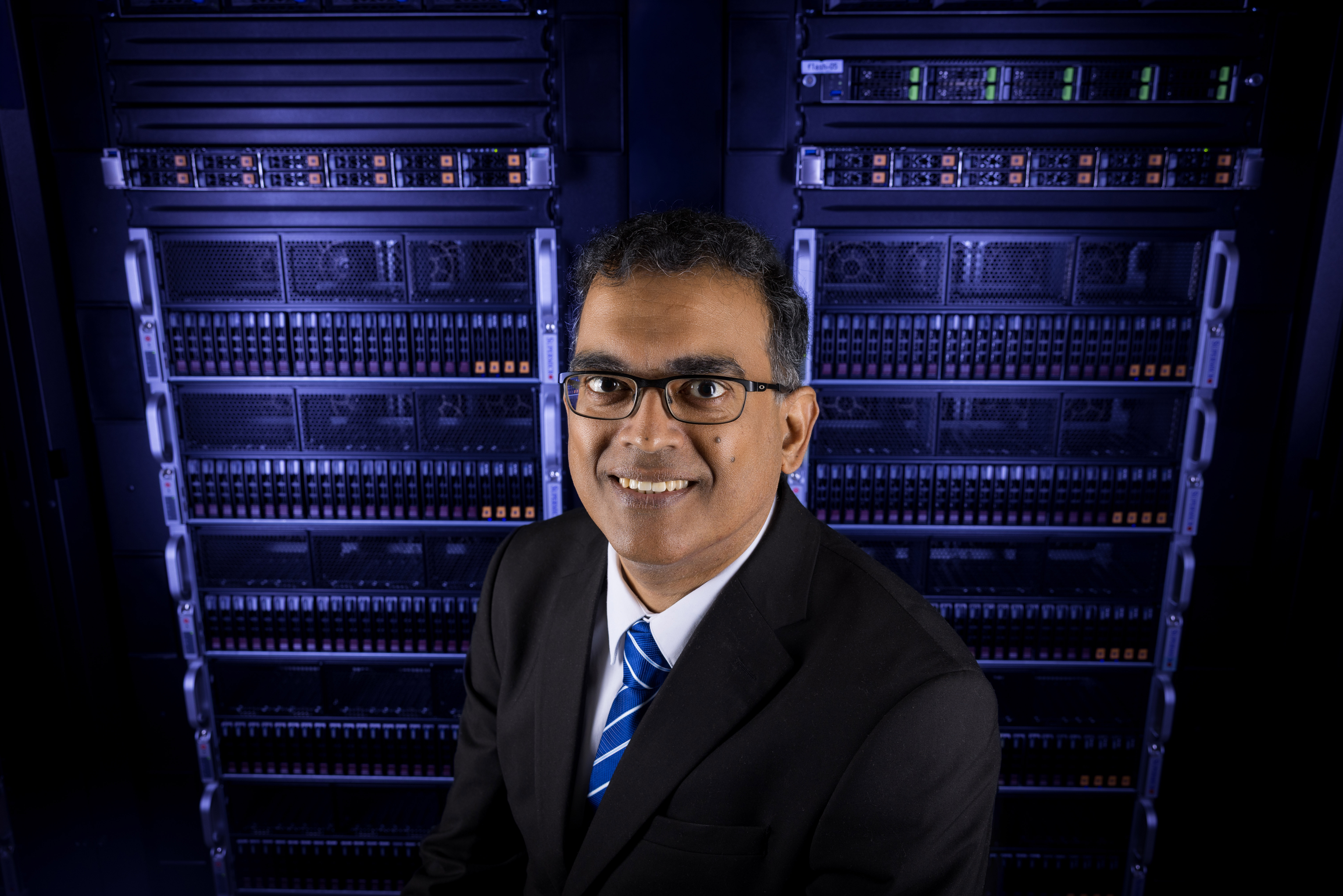 Byrav Ramamurthy, professor of computing at the University of Nebraska–Lincoln, stands in front of server racks in a blue-lit room.