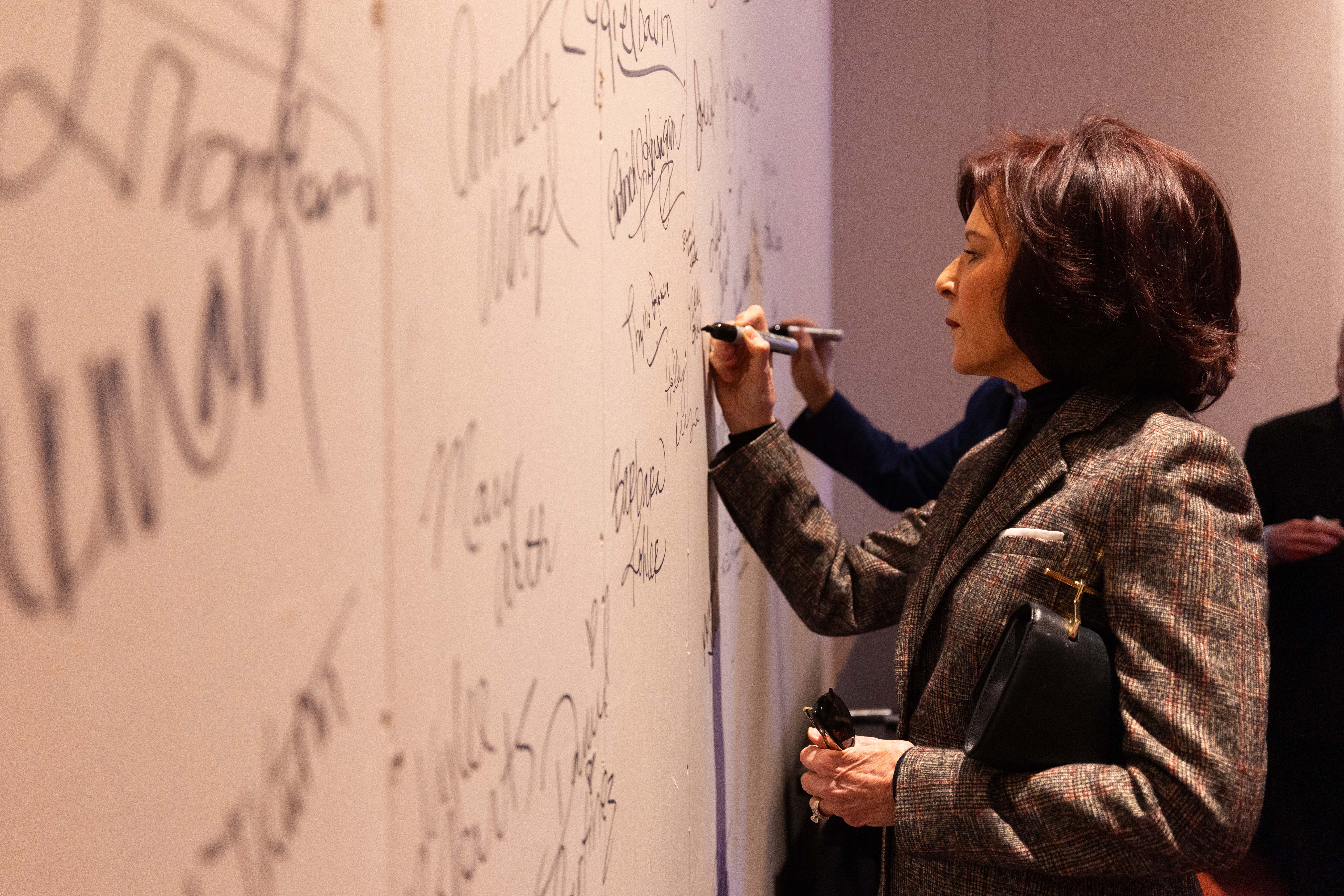 Vikki and Doug Kotil sign a temporary wall in a Lied Center for Performing Arts lobby.