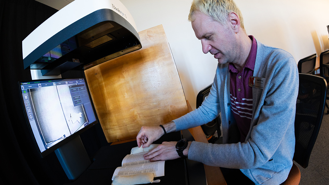 Zach Eden, a member of the Love Library collections maintenance and delivery team, weights a volume of Laurus so it lays open underneath a scanner. Eden is one of the staff members working on digitizing the library's archive of Laurus, a student-produced literature and art journal.