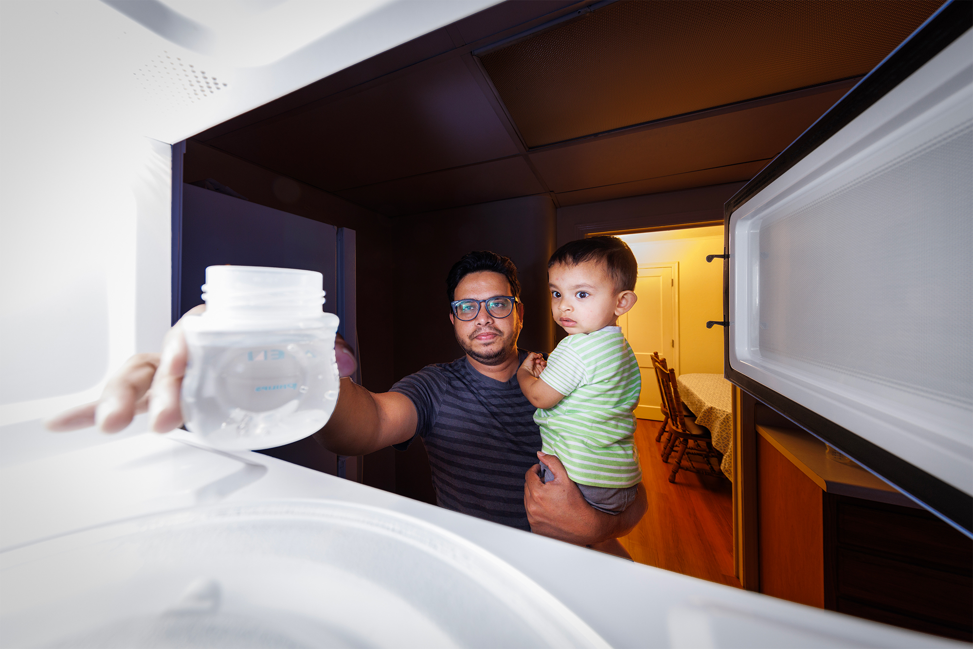 Kazi Albab Hussain holds his son while removing a plastic container from a microwave