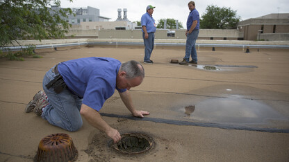 Bryan Ludemann (left) removes debris from a roof drain as Scott Hunt (right) and Scott Blair discuss possible roof repairs to UNL's Life Sciences Annex on East Campus. Spring rains have created a variety of unique challenges for UNL building systems maintenance employees.