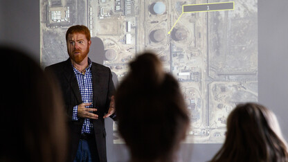 Tyler White teaches while illuminated by a large satellite image of an Iranian oil refinery. White, interim director of the National Security Studies program, recently earned the International Association for Intelligence Education's Instructor of the Year award.