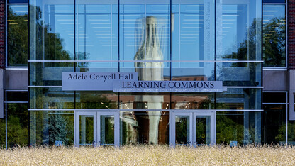 A reflection of the Green Point sculpture, Mueller Tower and Coliseum are distorted by the windows on the north side of the Adele Hall Learning Commons.