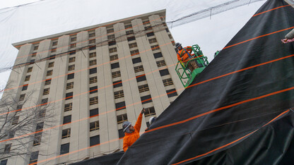Ark Wrecking employees hang a protective fabric over a mesh wall along 17th Street on Aug. 21 as part of preparations for the razing of Cather and Pound halls. The wall is designed to keep dust and debris from reaching Knoll Residential Center and Cather Dining Center. The residence hall towers are scheduled to be imploded at 9 a.m. Dec. 22.