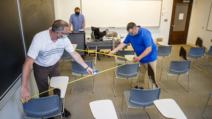 Jack Dohrman (left) and and Shawn Languis (right), use tape measures to gauge physical distancing needs within an Avery Hall classroom. Keith Derickson, a support manager with academic technologies, stands in the instructor position to assist with the mapping. Based on their measurements, seating in this classroom will shift from 35 desks in a regular semester to 14 in the fall. The change allows the university meet the six-foot social distancing needs related to COVID-19. In large lecture halls