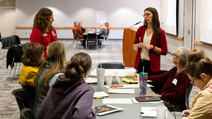 Seven women work at a table in a meeting room.