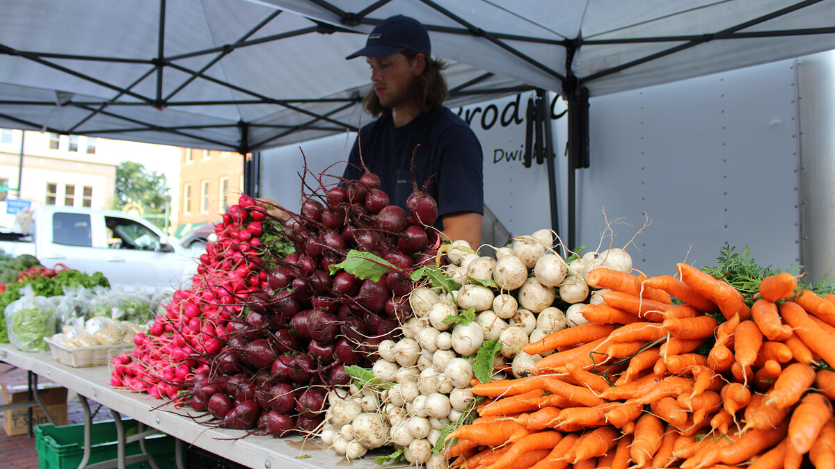 A young man stands behind a table stacked with vegetables.