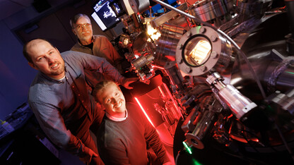 Craig Zuhlke, George Gogos and Graham Kaufman pose with the Leybold ultra-high vacuum laser surface processing and materials analysis system in the Engineering Research Center.