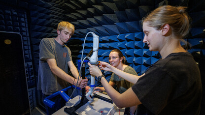 Sean Crimmins, Erika Smith and Rachael Wagner adjust the robotic arm on a stand in a chamber for electromagnetic compatibility and electromagnetic interference testing.