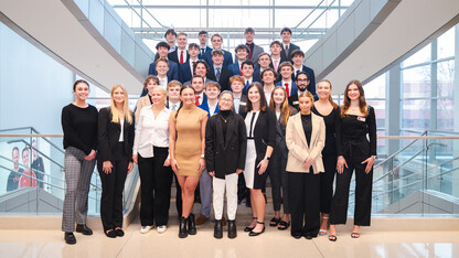 Thirty-four students in business attire pose on a staircase in Hawks Hall.