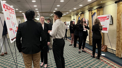 About a dozen college students stand next to their research posters in the Nebraska Governor's Mansion.