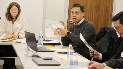 Jenny Mason, Zhenghong Tang and Yunwoo Nam sit at meeting tables. Tang holds a map.