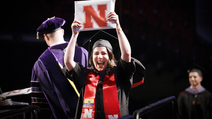 Graduate Karolayn Greys Chavez Loor smiles and holds her diploma above her head.