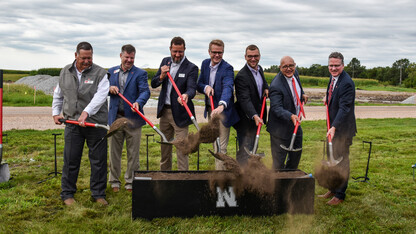 Seven men ceremonially shovel dirt.