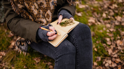 A woman in cold-weather garb with fingerless gloves writes in a journal.