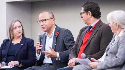 A man speaks into a microphone onstage next to another man and two women.