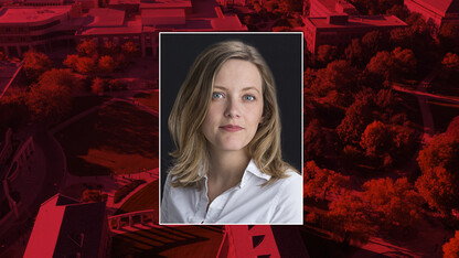 Color portrait of Sarah Walcott, Ardis B. James Curator of Collections at the International Quilt Museum, on a red campus background.