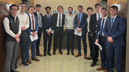 Twelve male students — all members of the Wall Street Scholars of Nebraska — stand in an office entryway in formal attire.