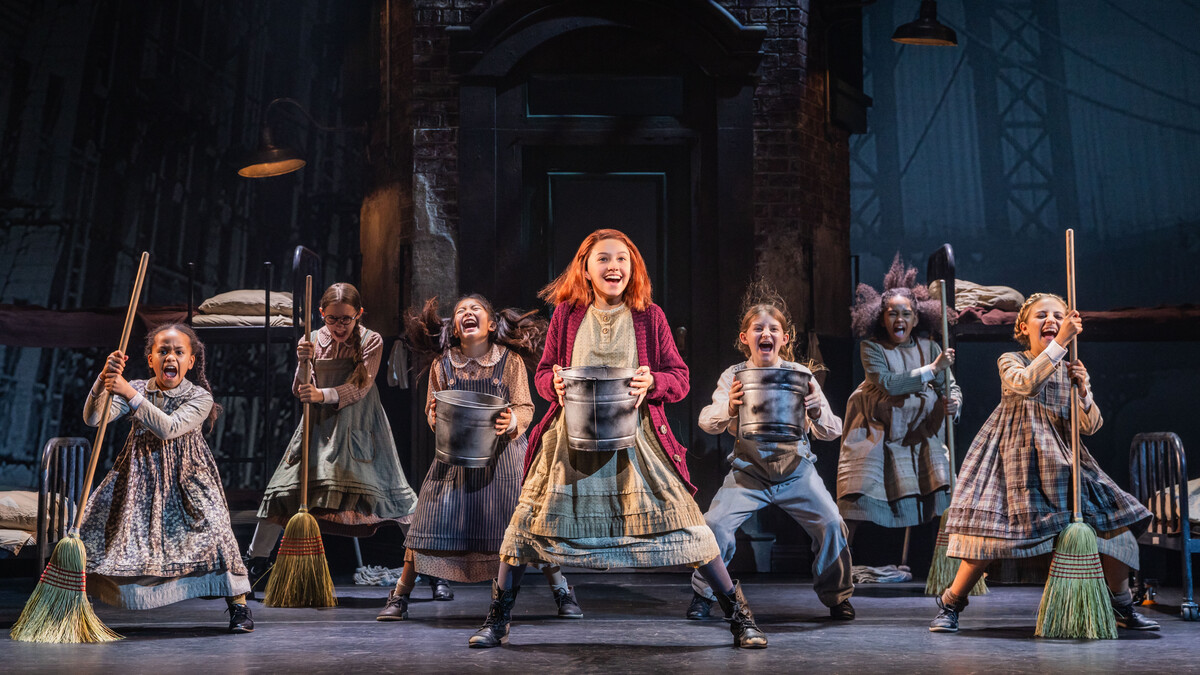 Seven orphan girls sing and dance with buckets and brooms in a scene from the musical "Annie."