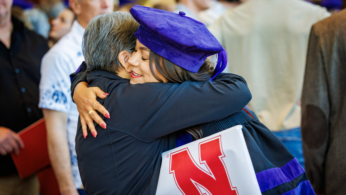 Law graduate Jori Peters, dressed in black and purple regalia, hugs a family member, diploma in hand.