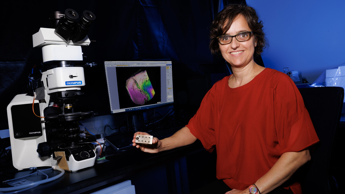 Lucia Fernandez-Ballester, assistant professor of mechanical and materials engineering, poses next to a microsope and computer monitor in a dimly lit lab.