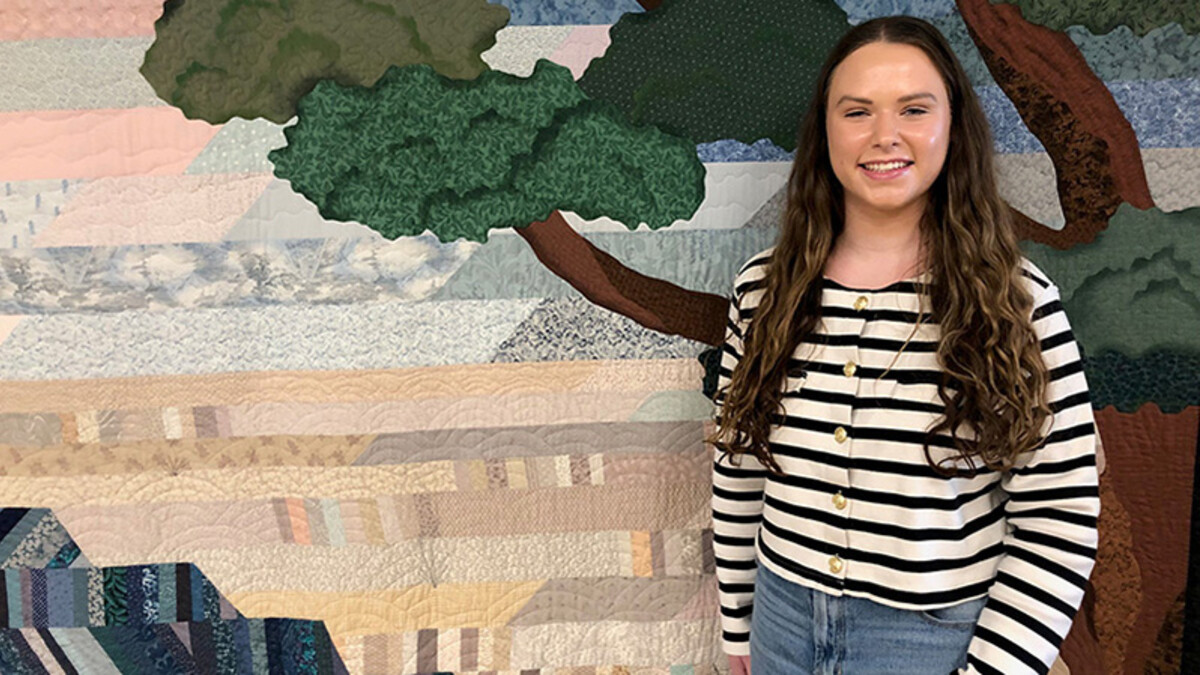 Brooklyn Buell, a white college student with long brown hair stands in a striped black and white sweater and jeans.